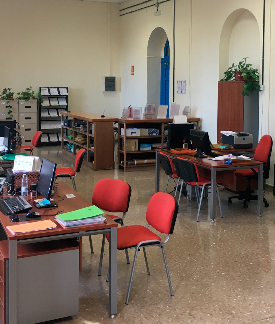 Imagen de la secretaría de la Facultad de Comunicación y Documentación, se ven diversos puestos de trabajo con sillas, mesas y estanterías