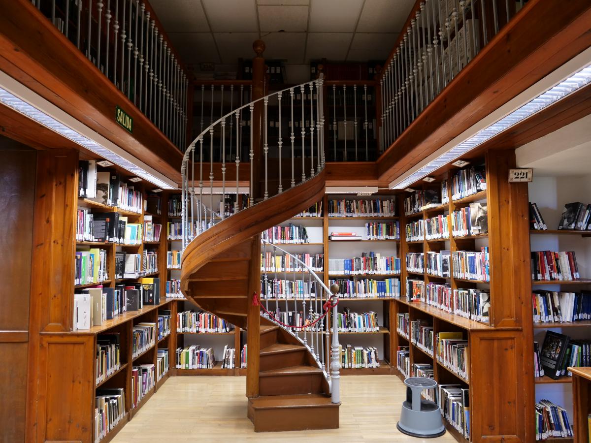 Escalera de caracol en biblioteca Colegio Máximo con estanterías al fondo.